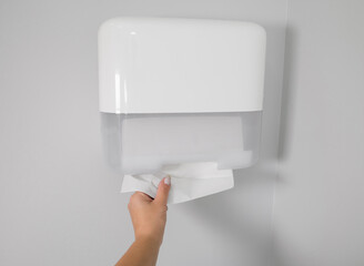 Woman taking new fresh paper towel from dispenser in bathroom,