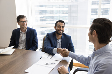 Happy young Indian project owner man shaking hands with investor on corporate meeting after...