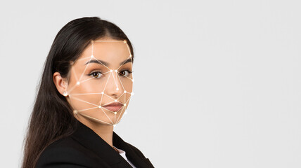 A woman stands confidently in a studio, with facial recognition technology overlays highlighting her features. The modern background enhances the focus on her expression and the technology used.