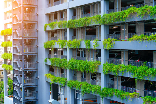 Multi-level parking on the floors with a ladder and green hanging ampelous plants of a multi-storey residential building.