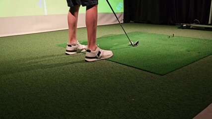 Golfer practicing swings indoors at a virtual golf simulator in a training facility during a summer afternoon