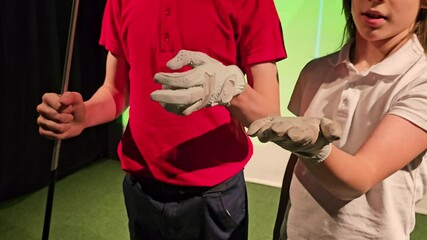 Two children practice golf swings indoors with a simulator at a sports center in the afternoon