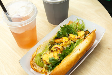 Delicious grilled shrimp sandwich with fresh vegetables and two refreshing drinks on a wooden table.