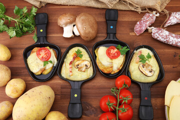 Delicious traditional Swiss melted raclette cheese served in individual skillets with salami and bacon