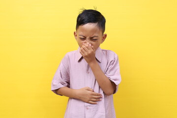 Asian little boy standing while grimacing in pain. He is suffering from stomach ache or diarrhea