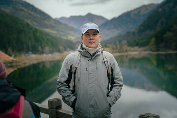 Fototapeta premium Hiker man wearing jacket and backpack standing by the mountain lake and looking at camera, Dagu Glacier, Chengdu, China.