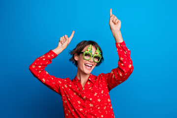 Photo of pretty young woman dance point fingers up empty space wear red christmas festive shirt isolated on blue color background
