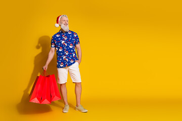 Fototapeta premium Full body portrait of stylish santa mall bags look empty space wear christmas print shirt isolated on yellow color background
