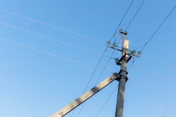 A power transmission pole with wires spreading out in various directions against a clear blue sky on a sunny day.