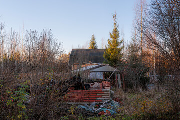 An old, decaying wooden structure surrounded by autumnal nature on an overgrown grassy lot,...