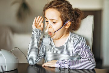 Sick little girl with cough doing inhalation at home with nebulizer inhaler mask. Asthma medicine. Flu season. Healthcare concept.