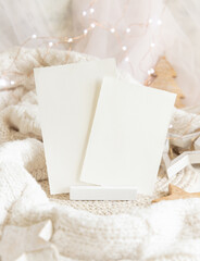 Vertical paper cards near white sweater and wooden Christmas decor and lights, mockup