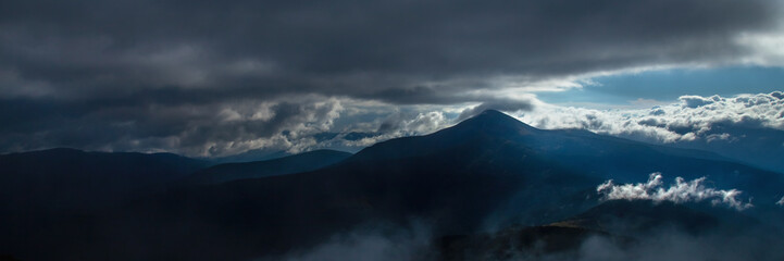 Fototapeta premium Fog and clouds in the mountains, clouds and nebula on mountain peaks. Beautiful nature. Horizontal image.