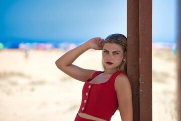 Young and beautiful Latin woman with long hair is leaning on a wooden poster on the beach. In the...