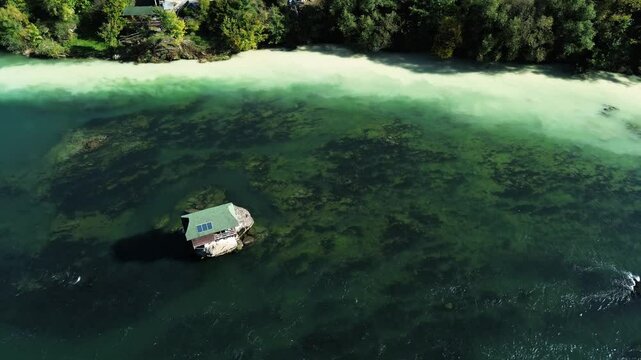 On a small rocky ledge in the middle of the winding Drina River with clear turquoise water, on the border of Serbia and Bosnia, beautiful and picturesque little wooden house. Aerial drone view.