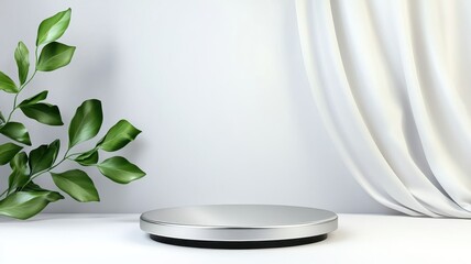 A sleek, silver stand on a minimalistic surface next to green leaves and draped fabric, creating a modern and elegant aesthetic.