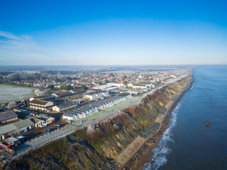 Fototapeta premium Aerial view of a frost and cold morning on the Suffolk, UK coast. Holiday homes and holiday chalets are above the cliff edge looking out to a cold North Sea.