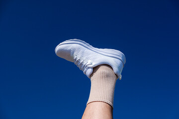 male leg on the background of the sky. White sneakers and blue sky