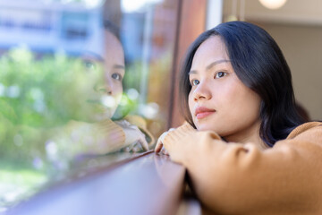 Young woman wearing a sweater sits by the window looking at the bright landscape, the warm...