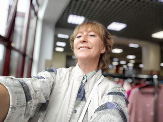 Middle-aged woman shopping happily in a store full of clothes during a bright afternoon