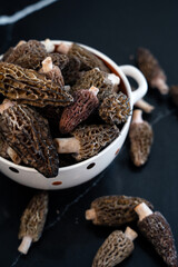 Obraz premium Close up of gourmet morel mushrooms in a white bowl on a dark background. These delicate mushrooms are prized in culinary dishes for their rich, earthy flavor and unique texture