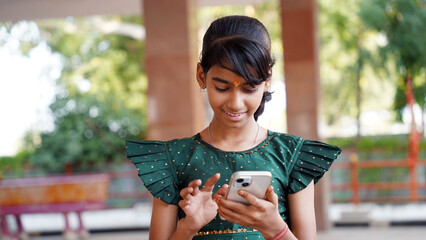 Front view of a happy Indian girl writing message or chat in smartphone or mobile