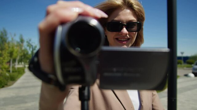 A young woman is filming a video outdoors using a camcorder on a bright sunny day, pov video of filming backstage, retro vintage mini dv camera.