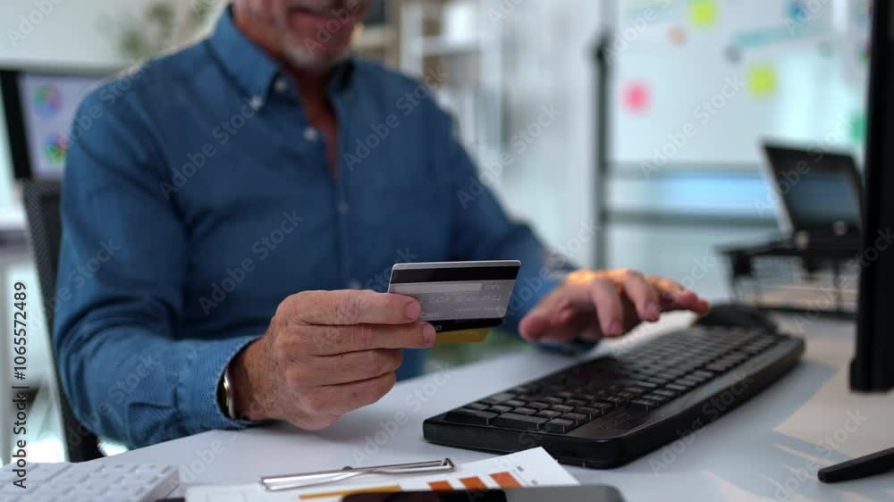 Poster manager holds a credit card while typing on a keyboard, processing an online payment in a business o