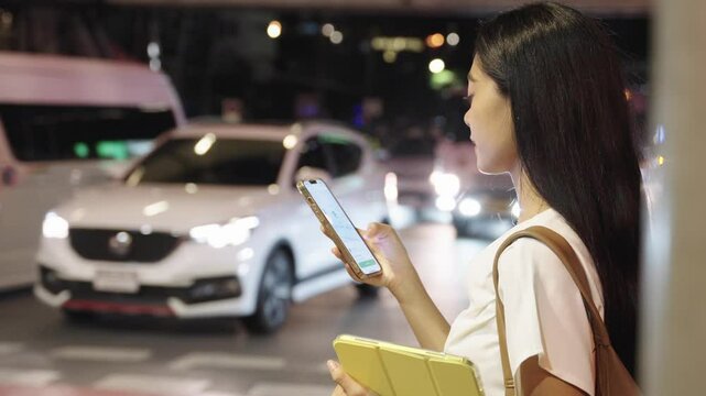 Businesswoman ordering taxi using smartphone app at night in bangkok. Bangkok night lifestyle