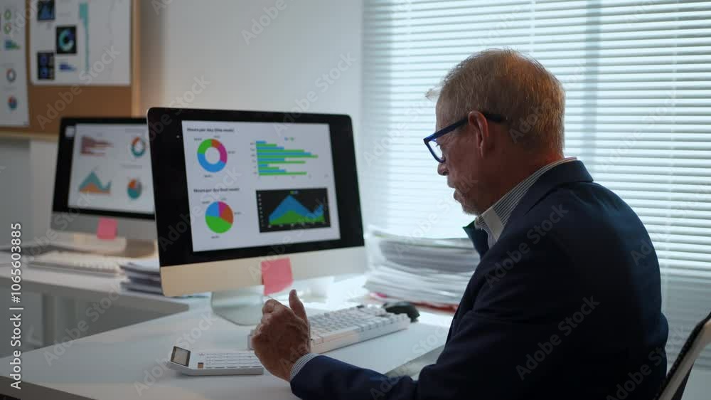 Poster businessman sitting at a desk, explaining charts and data displayed on a computer screen during a pr