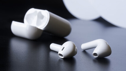 A pair of white wireless headphones with a white charging case on a dark background. Selective...