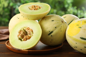 Fresh whole and cut honeydew melons on wooden table against blurred green background, closeup