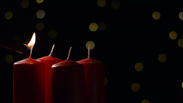 Hand lighting first red candle in the Advent wreath on a festive background with golden decorations, close up shot. Holiday and tradition concepts.