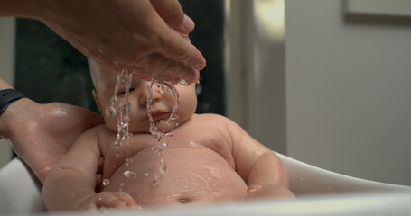 Fototapeta premium Water gently pouring from hand over baby’s belly during bath, baby calm and relaxed, focused on nurturing bath care. 800 fps slow-motion