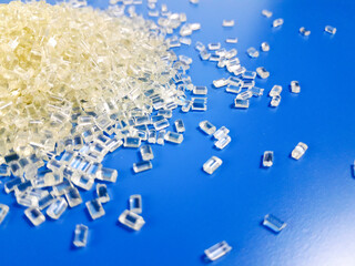 Transparent polycarbonate plastic granules on a blue background, one of the basic materials in the...