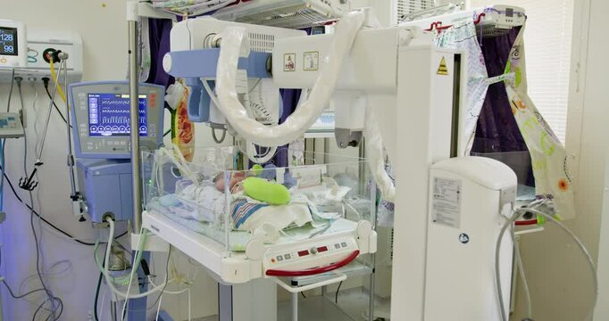 Newborn baby receiving intensive care in neonatal unit with incubator and monitoring equipment. High-tech medical devices surrounding infant. Healthcare professionals ensuring optimal care.