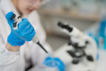 Close-up of gloved hand using micropipette dropping liquid into petri dish, conducting experiment...