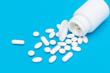 Global Pharmaceutical Industry and Medicinal Products - White Pills or Tablets Scattered from the Pill Container, Lying on Blue Background