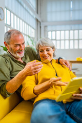Senior couple reading online news together on the sofa