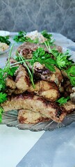 a festive table with food, in the center a large plate with fried meat, including fried sausages and chicken drumstick, the dish is decorated with greenery, 
