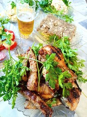 a festive table with food, in the center a large plate with fried meat, including fried sausages and chicken drumstick, the dish is decorated with greenery, a glass of beer is visible against the back