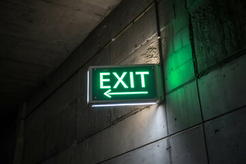 A glowing green exit sign points left within a dimly lit corridor, indicating a safe way out.