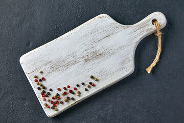 white wooden cutting board with scattered peppercorns on black stone table. top view with copy space