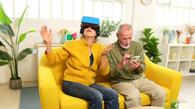 Senior woman using virtual reality googles next to her husband sitting on the sofa using mobile phone