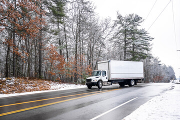 Middle duty day cab rig white semi truck transporting cargo in box trailer turning on the winter...