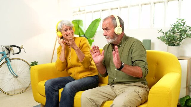 Cute senior couple listening to music together and dancing sitting on the sofa indoors