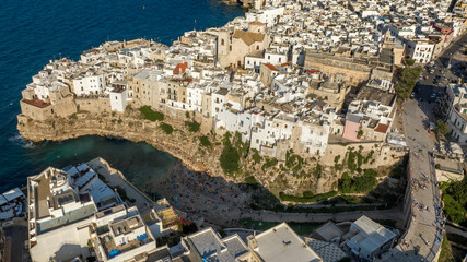 Naklejka premium Aerial view at sunset of the historic center of Polignano a Mare, in the province of Bari, Puglia, Italy. In foreground is Lama Monachile beach, the most important and famous beach in town.
