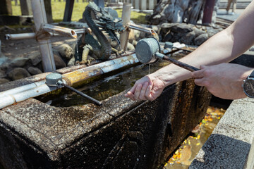 A tourist is holding a ladle of water to wash his hands before going to a shrine in Japan as a...