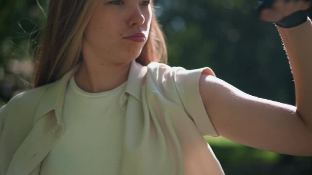 Close-up of woman flexing her arm in strong, confident pose, wearing biker gloves, with green, blurred natural background, her expression and pose convey empowerment