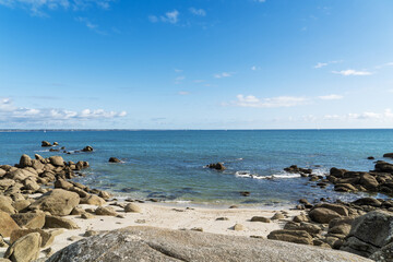 Paysage côtier de Beg Meil : le sable doré se mêle aux rochers sous un ciel bleu ponctué de nuages blancs.